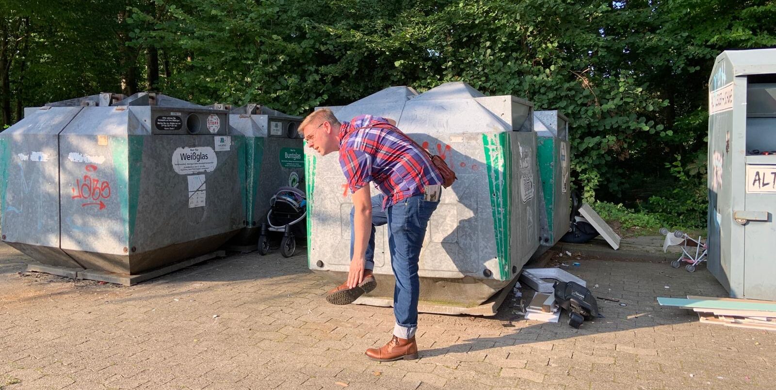 Ein Mann steht vor einem Altglascontainer. Neben dem Container liegt Müll auf dem Boden.