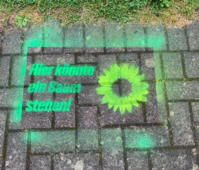 Text "Hier könnte ein Baum stehen!" und ein Sonnenblumen Logo mit Sprühkreide auf einen Weg gesprüht.